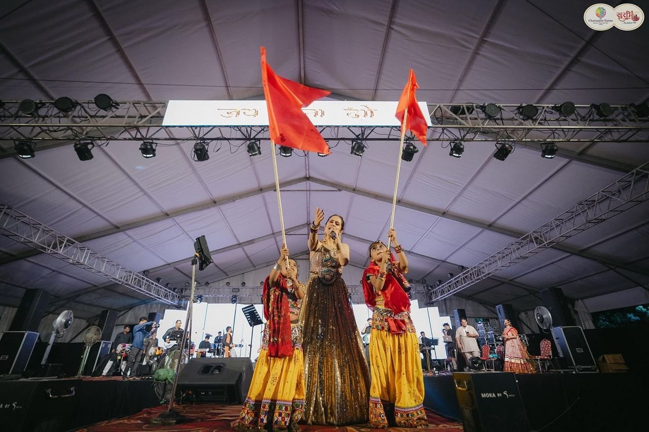 Singer with children waving red flags on stage at Surbhi Garba Dhoom Dandiya 2025, Chattarpur Farms, Nagpur